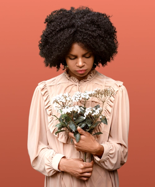 Black female model in cream colore retro style dress holding white flowers in her hands